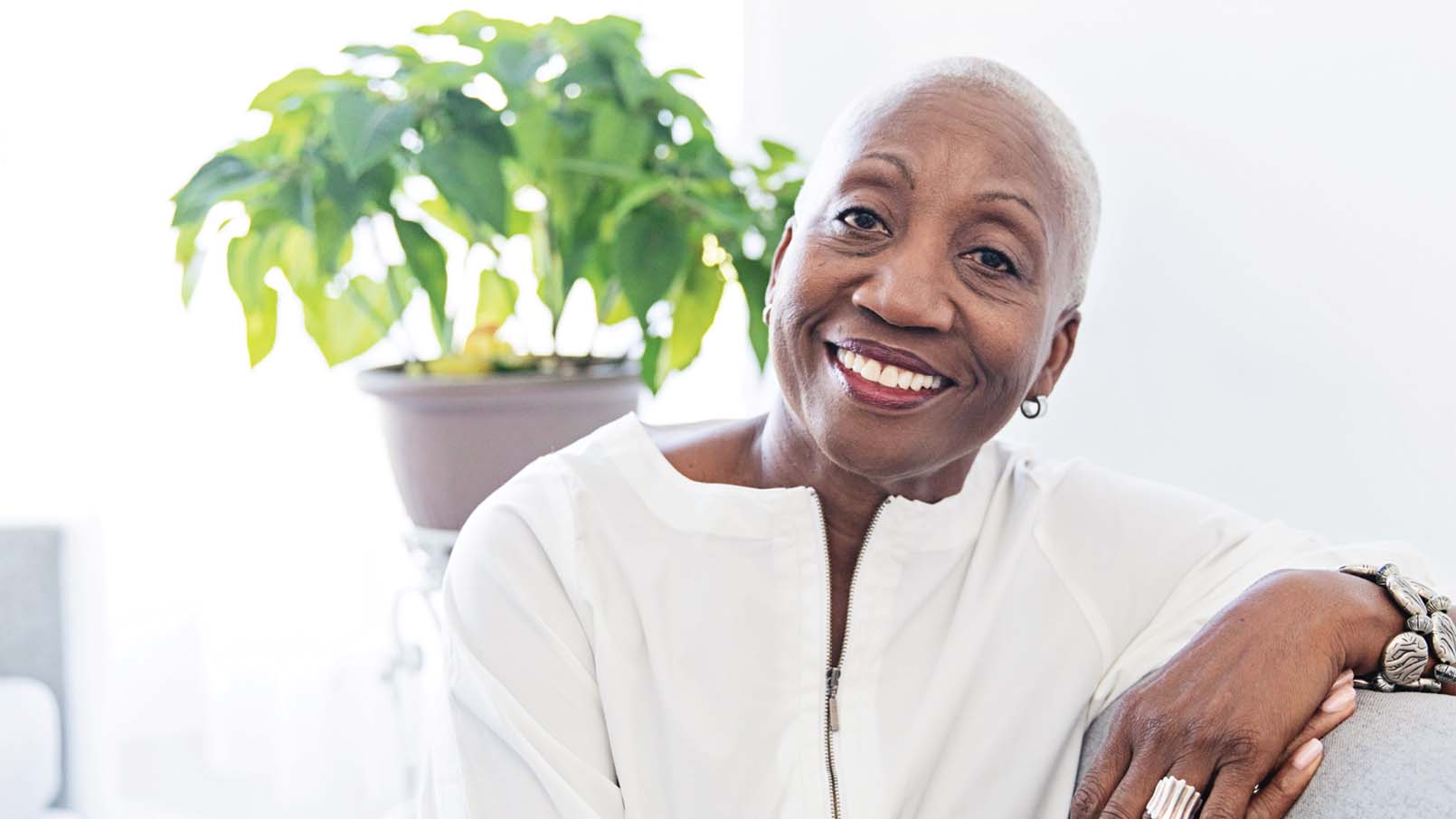 African American woman looks into the camera smiling with a potted plant behind her.