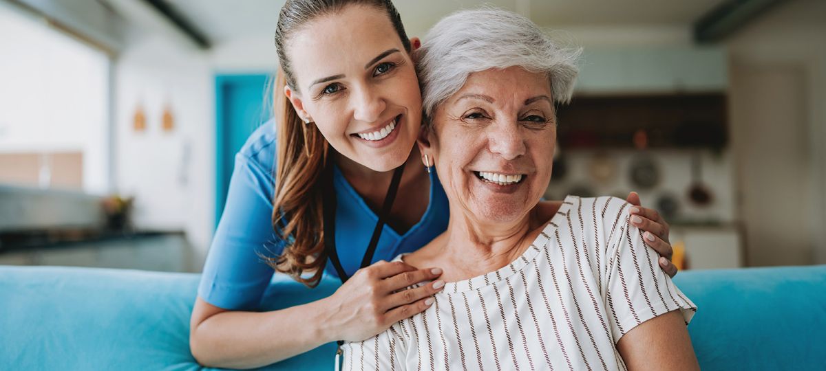 Two women, a doctor and a patient, sitting together smiling in a clinical setting.