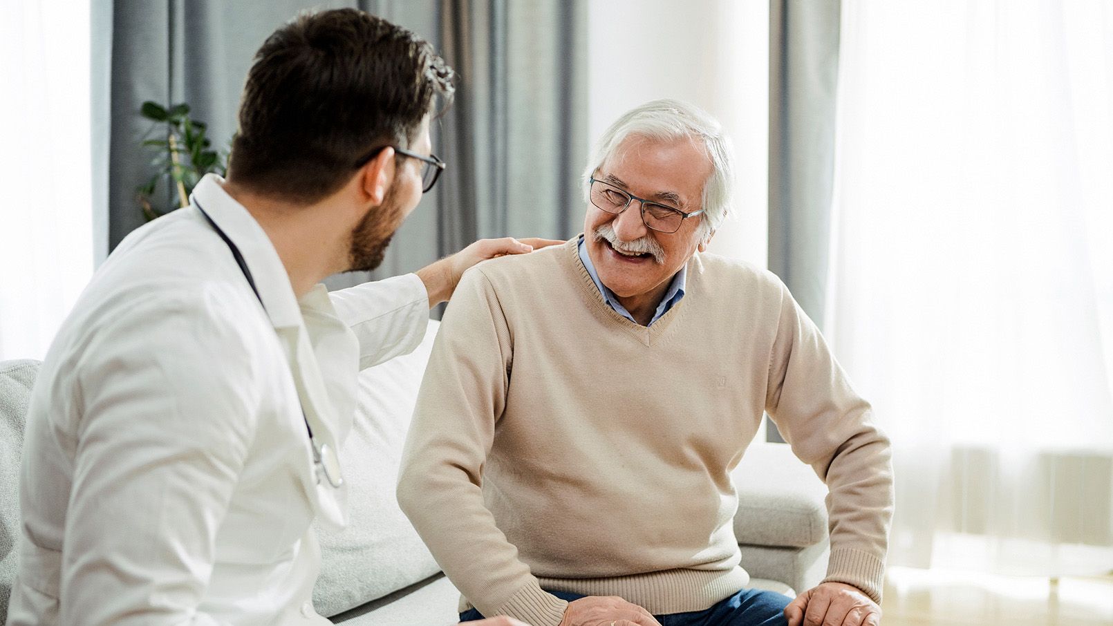 Older man sitting with his son in an apartment, both smiling and enjoying a conversation.