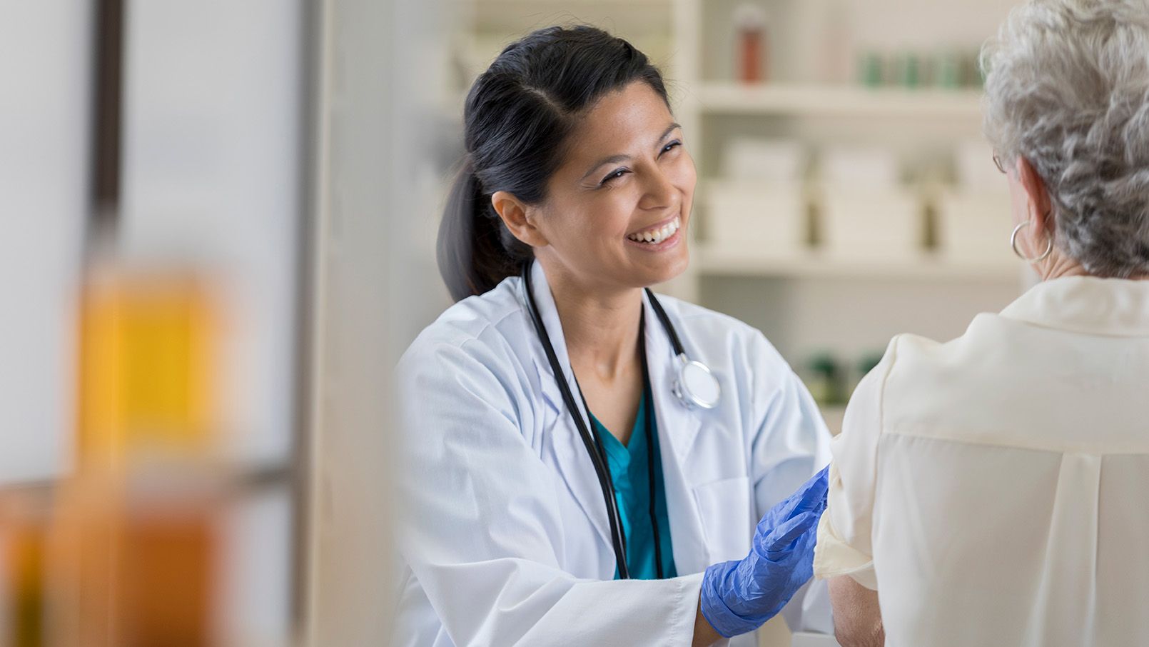 Female pharmacist talking with an older patient in a clinical setting.