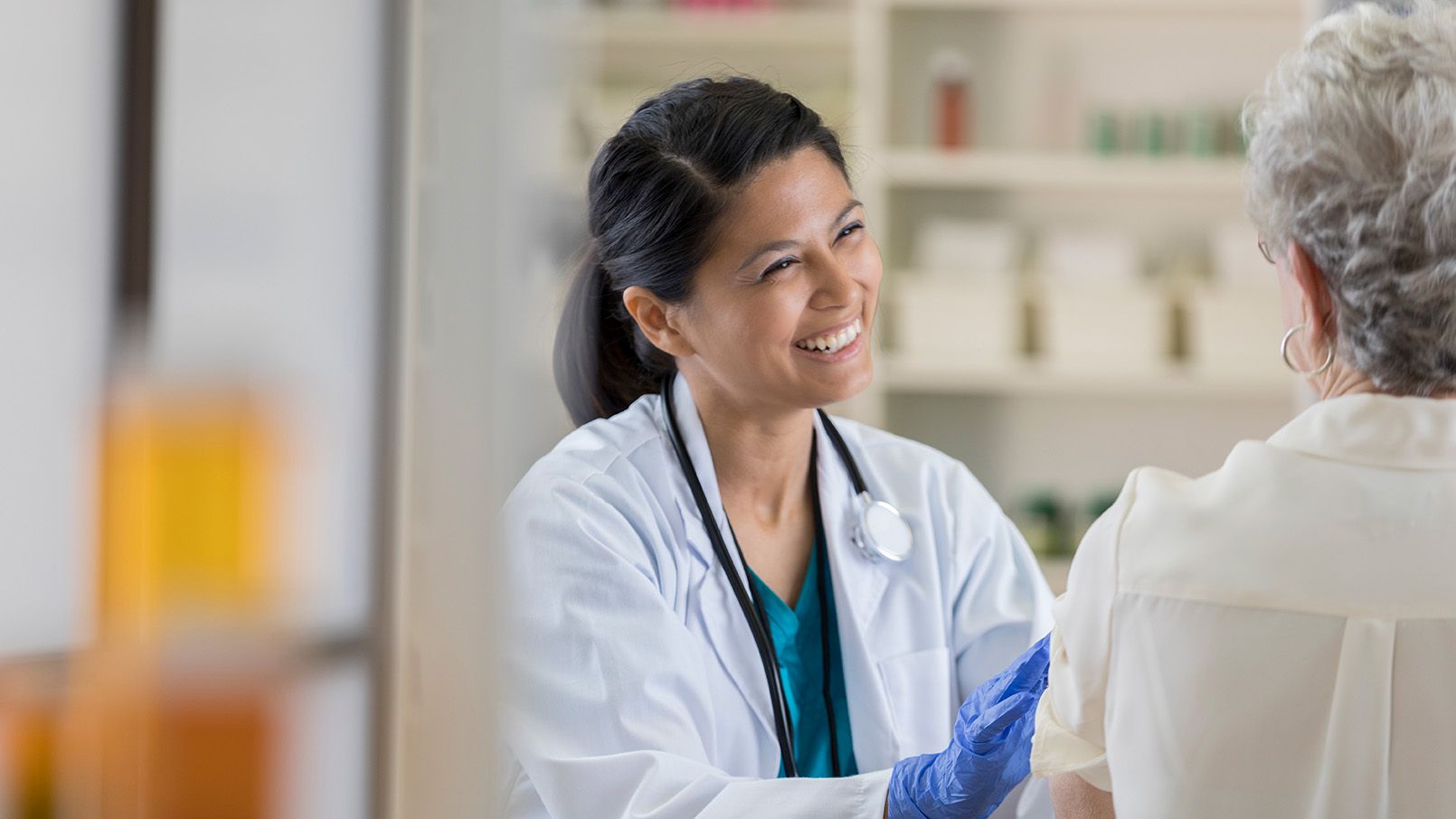 Doctor smiling and talking with an Erickson Senior Living patient during a check-up in a bright medical office.